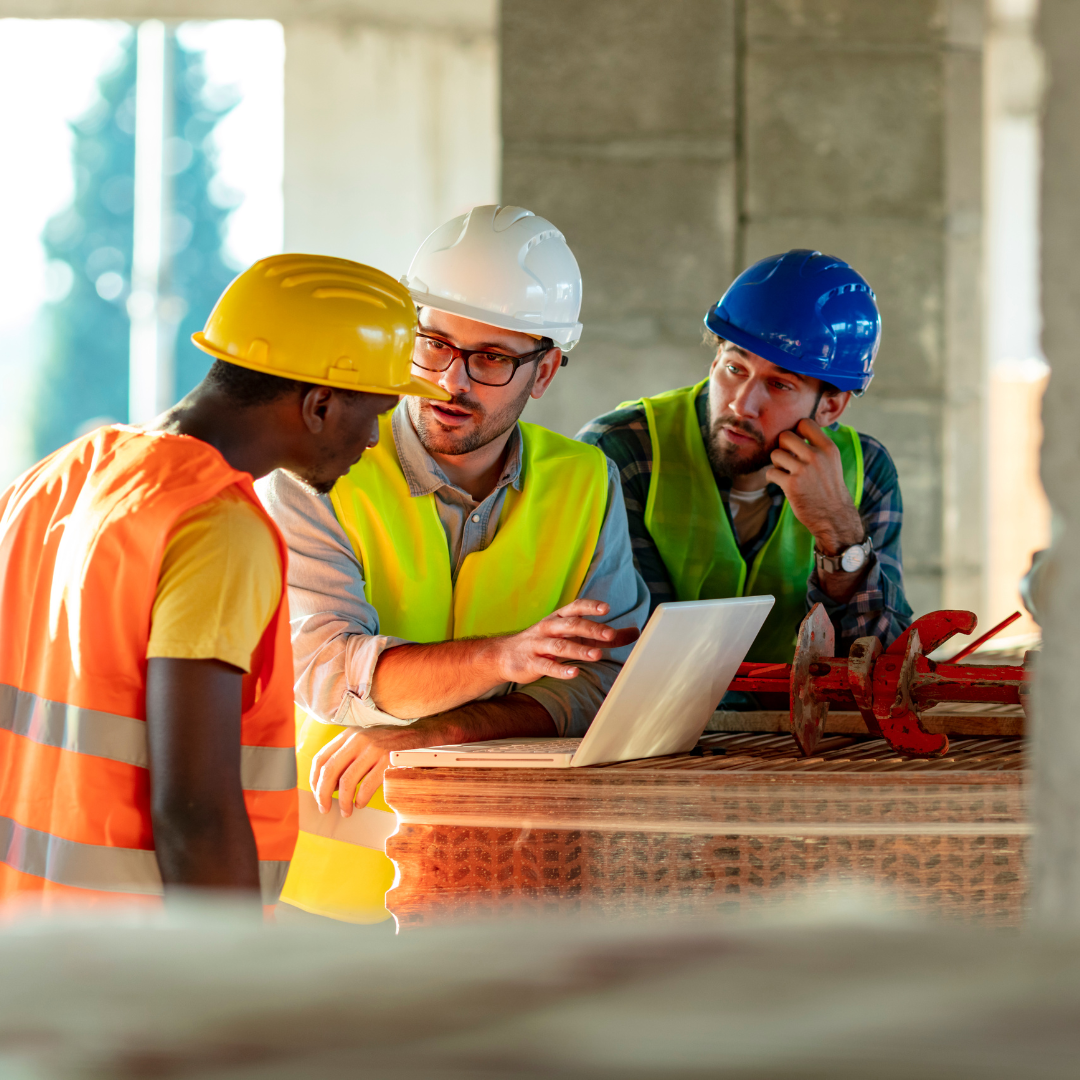 Group of construction workers stood around a laptop during a site meeting